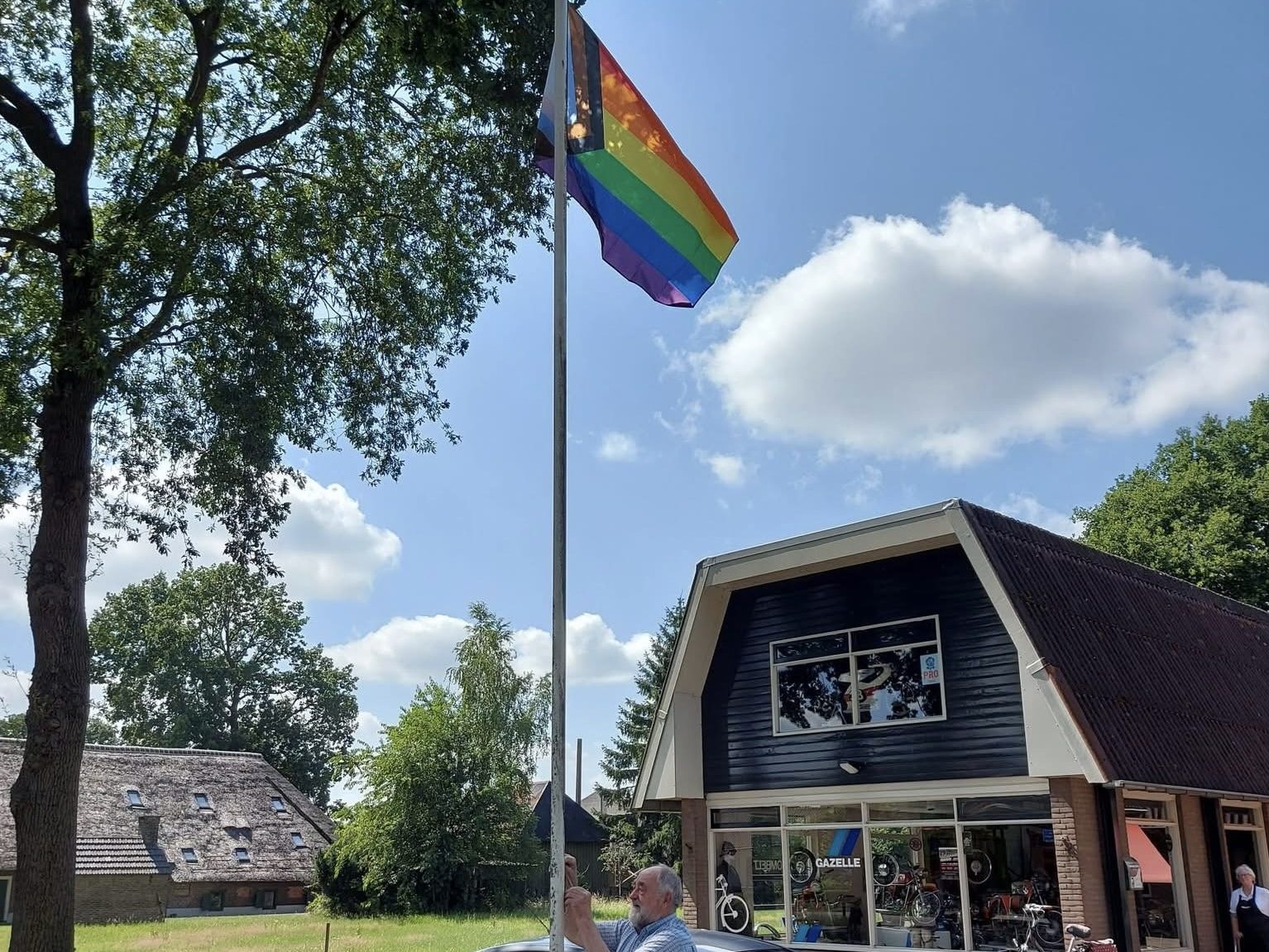Jan Zoombelt hijst een nieuwe progress-pride-vlag aan de mast voor zijn bedrijfspand