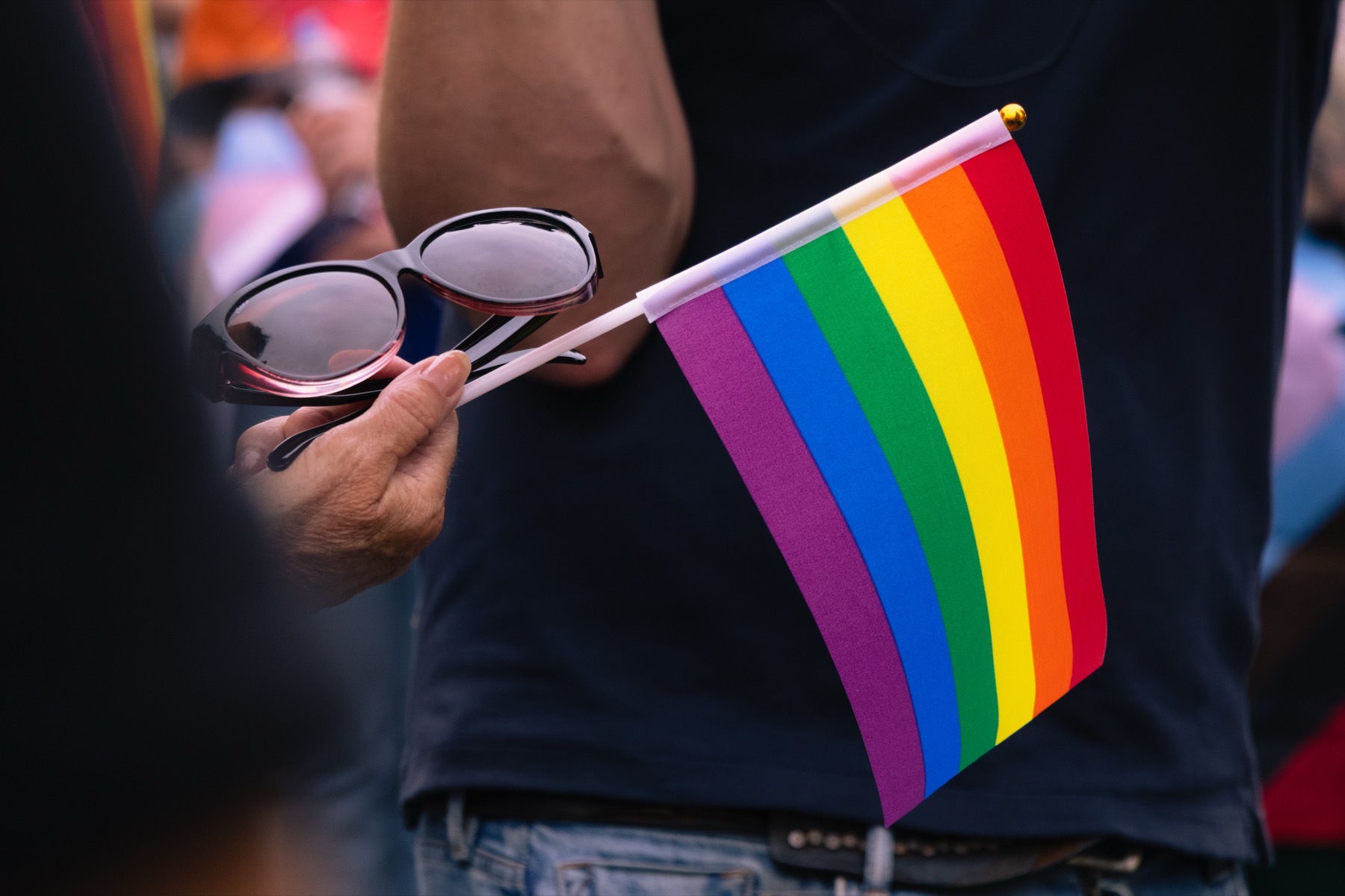 Een hand met zonnebril en een klein pride-vlaggetje