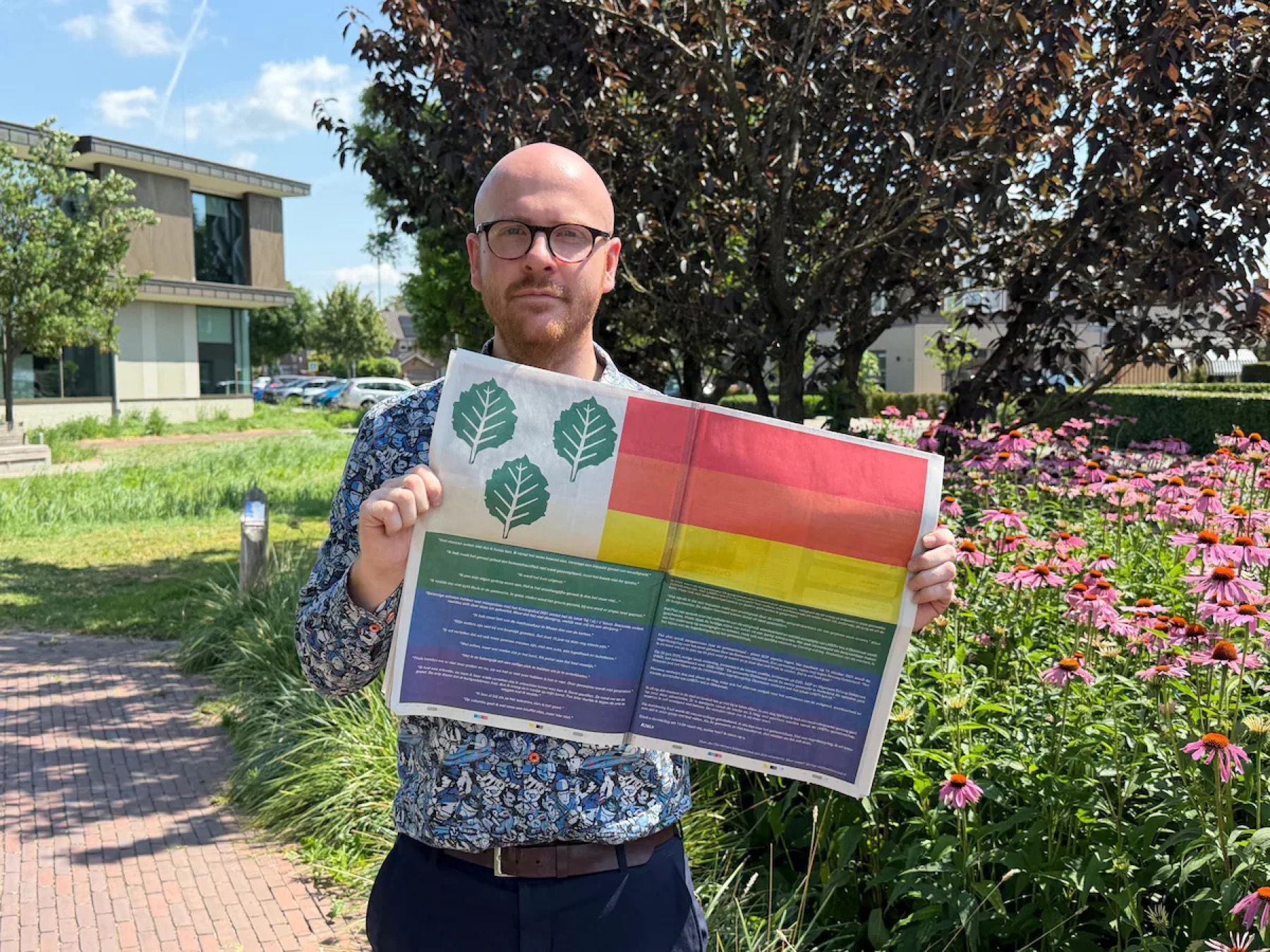 Kjeld Mooi houdt de krant open met daarin de paginagrote regenboogadvertentie
