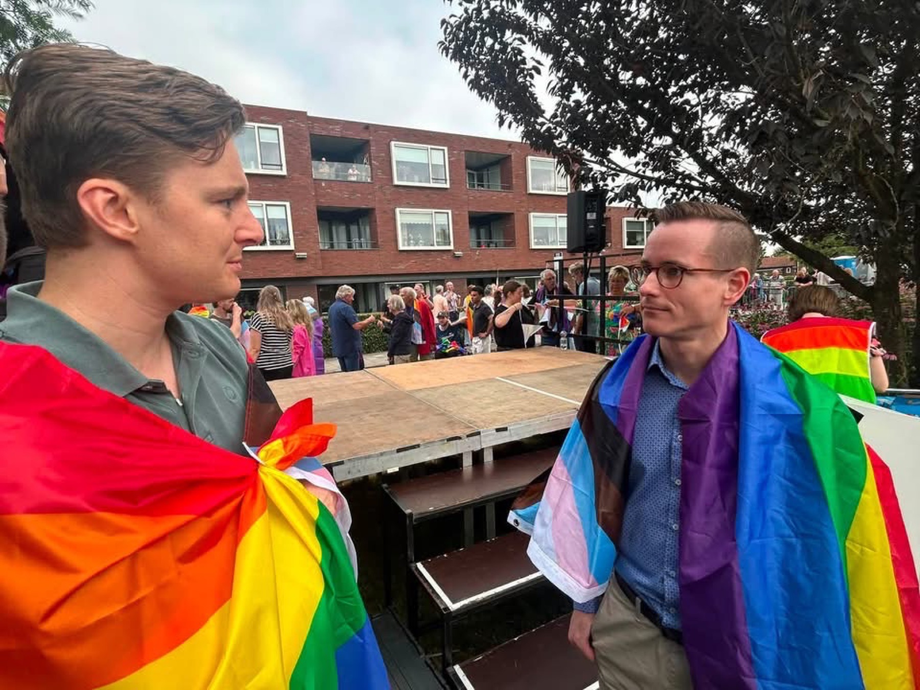 Twee mannen gehuld in regenboogvlaggen in gesprek bij een podium